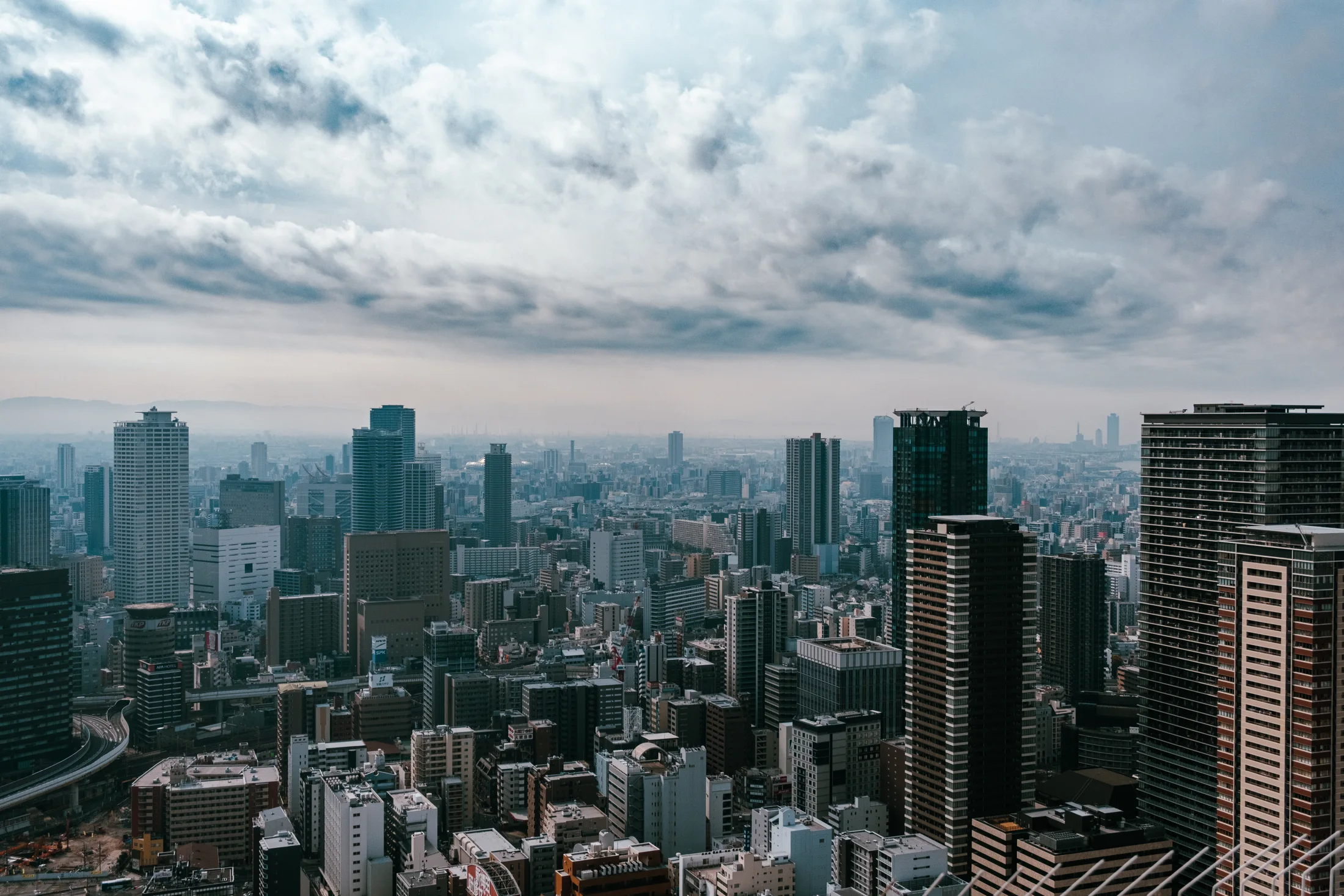 A dense city skyline seen from above beneath large gray and white clouds.
